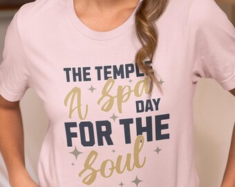 May include: A pink t-shirt with the text "The Temple A Spa Day For The Soul" in gold and navy blue lettering with small stars around the text.