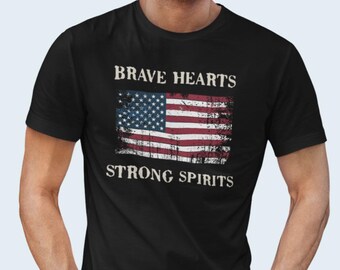 Può includere: T-shirt nero con una grafica di bandiera americana usurata e il testo "Brave Hearts Strong Spirits".