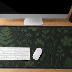 May include: A rectangular desk mat featuring a dark green background with a botanical pattern of various green leaves and flowers. A white keyboard and mouse are on the mat. A computer monitor is above the mat.