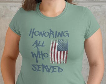 Può includere: Una maglietta verde chiaro con il testo "HONORING ALL WHO SERVED" in blu e una grafica di bandiera americana usurata.