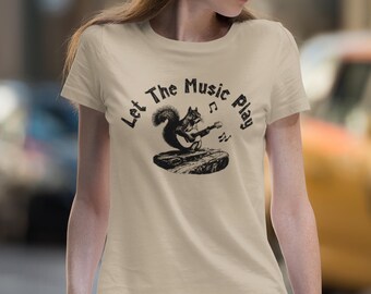Puede incluir: Una camiseta beige con un gráfico negro de una ardilla tocando la guitarra. El texto "Let The Music Play" está impreso en la camiseta.