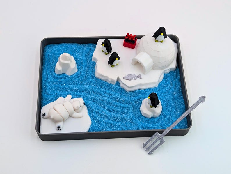 May include: A miniature arctic scene in a black tray, featuring a blue sandy sea, icebergs, and an igloo. Includes a polar bear, penguins, and a trident. The scene is a playful, decorative item.