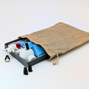 May include: A gray metal box containing a miniature polar scene with a white igloo, polar bear, and penguins. A burlap bag is partially open, revealing the contents. The scene includes red and blue accents.