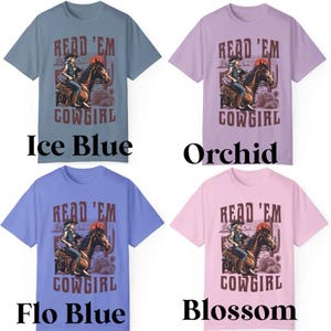 Może przedstawiać: Cztery koszulki w kolorach lodowego błękitu, orchidei, flo blue i blossom. Każda koszulka zawiera grafikę kowbojki na koniu z napisem "READ 'EM COWGIRL". Projekt obejmuje pustynny krajobraz i zachodzące słońce.