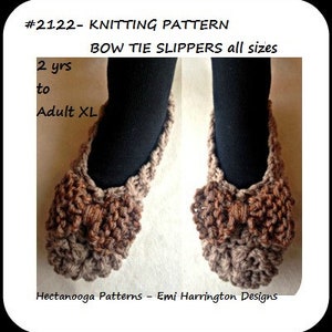 Op de afbeelding: Een paar bruine gebreide strik-pantoffels. De pantoffels zijn gemaakt van een dik garen en hebben een strikdetail aan de bovenkant. De afbeelding bevat de tekst "#2122- KNITTING PATTERN BOW TIE SLIPPERS all sizes 2 yrs to Adult XL".