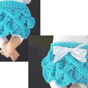 May include: A turquoise crochet skirt with a scalloped design. The skirt has a white and light blue striped bow. The skirt is shown on a baby doll. The skirt is a baby clothing item.