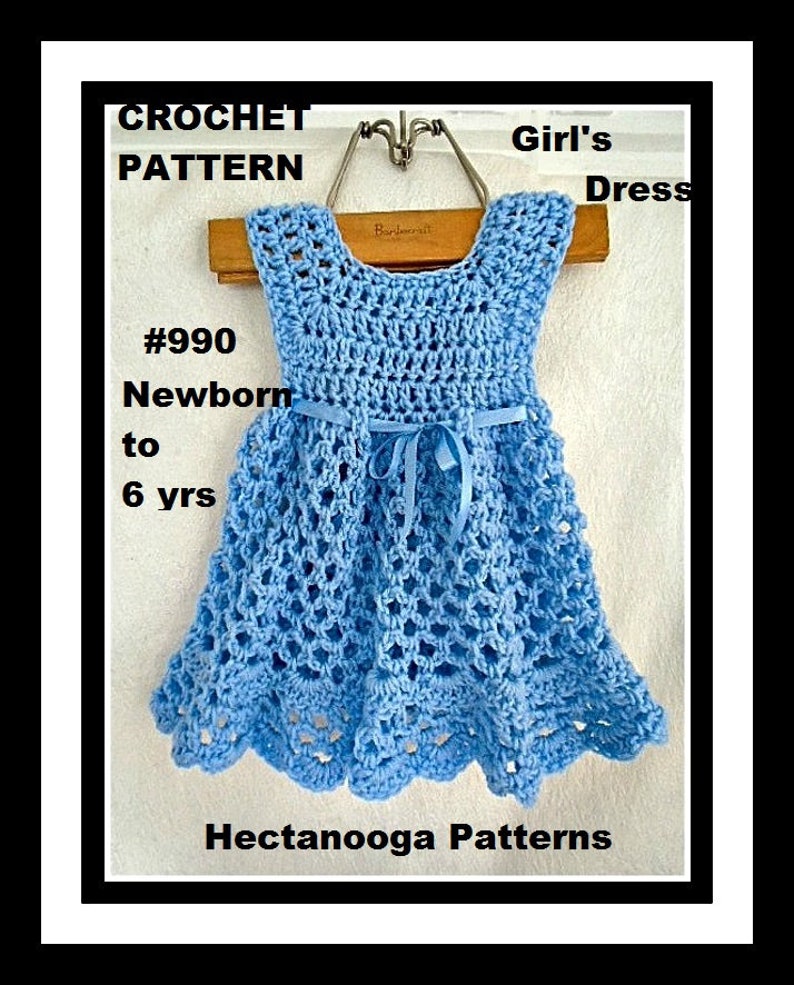 Pu&ograve; includere: Schema a uncinetto per un vestito da bambina, #990, neonato a 6 anni. L'abito &egrave; azzurro chiaro con un motivo a uncinetto bianco e un nastro blu.