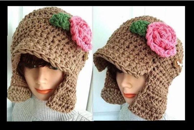 May include: A brown crocheted hat with a wide brim and ear flaps. The hat is decorated with two pink and green fabric flowers.