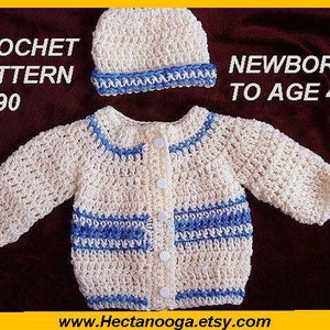 May include: A cream-colored crochet baby sweater and matching hat with blue trim. The sweater has a button-up front and blue stripes. Text on the image reads "CROCHET PATTERN #490" and "NEWBORN TO AGE 4".