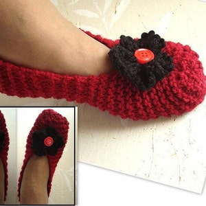 May include: Red knitted slippers with a black flower and a red button. The slippers are shown on a white background.