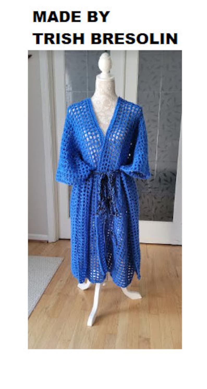 Pode incluir: Uma bata de croch&ecirc; azul com cinto de la&ccedil;o. A bata est&aacute; em um manequim branco e o texto "MADE BY TRISH BRESOLIN" est&aacute; na parte superior da imagem.