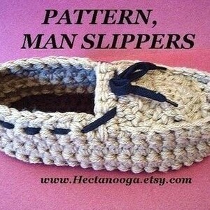 Puede incluir: Una zapatilla de ganchillo beige con detalles y cordones azul oscuro. El texto "PATTERN, MAN SLIPPERS" est&aacute; en la parte superior y "www.Hectanooga.etsy.com" en la inferior. La zapatilla est&aacute; sobre un fondo rosa.