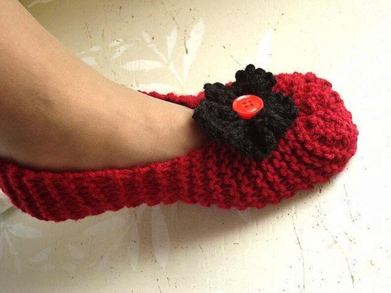 May include: Red knitted slipper with a black fabric flower and a red button in the center.