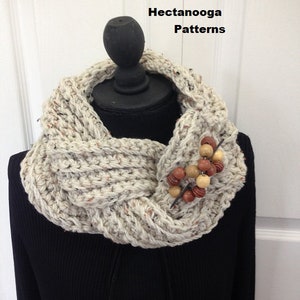 May include: A crocheted cowl in a beige color with a brown and beige beaded embellishment. The cowl is displayed on a black mannequin. The text #2871 crochet pattern BRAIDED COWL Hectanooga Patterns is visible at the top of the image.