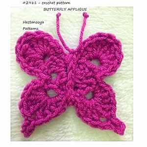May include: A crocheted butterfly applique in a bright pink color. The butterfly has a detailed design with openwork and a pair of long antennae.