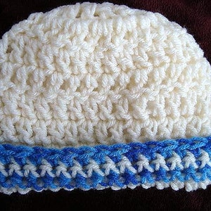 May include: A crocheted beanie hat. The main body of the hat is a creamy white color, with a textured stitch pattern. The brim is a contrasting blue and white, adding a pop of color. The hat is handmade and suitable for cold weather.