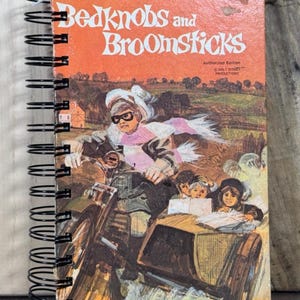 May include: A spiral-bound notebook featuring the cover of "Bedknobs and Broomsticks." The cover art depicts a woman riding a motorcycle with children in a sidecar. The title is in orange, with the words "Walt Disney Productions" above.