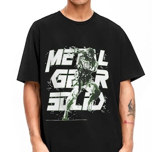 May include: Black t-shirt with a white graphic print of a character from the video game Metal Gear Solid. The graphic includes the text "Metal Gear Solid" in white.