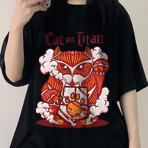 May include: Black t-shirt with a graphic of a red and orange cat with a white smoke cloud behind it. The text "Cat on Titan" is printed in white above the cat.
