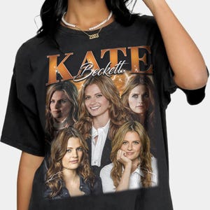 Puede incluir: Camiseta negra con un gráfico de estilo vintage de Kate Beckett de la serie de televisión Castle. El gráfico presenta cuatro imágenes de Kate Beckett en diferentes poses, con el texto "Kate Beckett" en una fuente naranja en negrita.