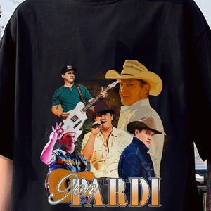 Puede incluir: Una camiseta negra con un estampado gráfico de cuatro cantantes de música country. Los cantantes llevan sombreros de vaquero y sostienen guitarras. El texto "Jon Pardi" está impreso en letras grandes de color amarillo en la camiseta.