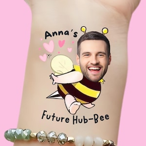 Può includere: Un tatuaggio temporaneo raffigurante un'ape dei cartoni animati con il volto di un uomo, strisce gialle e nere e la scritta "Anna's Future Hub-Bee". Sono visibili anche cuori rosa e un braccialetto.