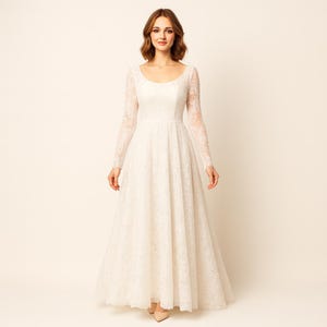 May include: An ivory wedding dress with a scoop neckline and long lace sleeves. The floor-length gown has a fitted bodice and a full skirt. The dress is made of a delicate lace fabric, creating an elegant silhouette.