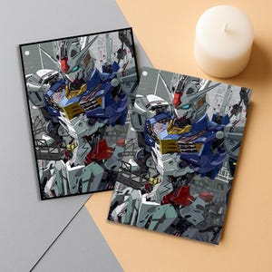 May include: Two framed prints featuring a detailed illustration of a robot with blue, white, red, and gold accents. The robot is set against a backdrop of industrial structures. A white candle sits nearby on a beige and gray surface.
