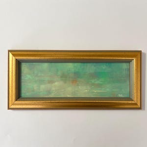 May include: A rectangular framed painting with a gold-colored frame. The artwork features a green and teal abstract landscape with hints of orange and brown. The painting is mounted on a white wall.