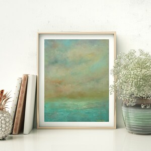 Puede incluir: Impresi&oacute;n art&iacute;stica de paisaje abstracto en un marco de madera clara. La obra presenta una escena serena con un mar turquesa, un horizonte marr&oacute;n dorado y un cielo nublado. Una pi&ntilde;a decorativa y libros est&aacute;n a la izquierda, y un jarr&oacute;n de flores blancas a la derecha.