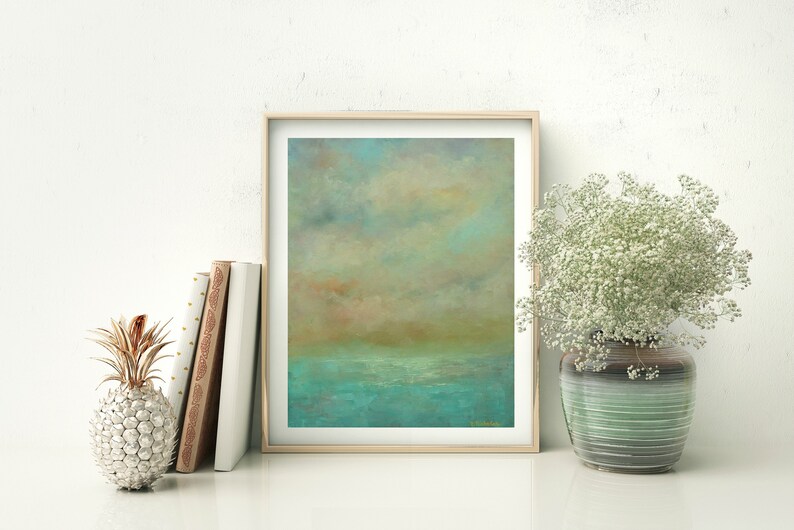 Puede incluir: Impresi&oacute;n art&iacute;stica de paisaje abstracto en un marco de madera clara. La obra presenta una escena serena con un mar turquesa, un horizonte marr&oacute;n dorado y un cielo nublado. Una pi&ntilde;a decorativa y libros est&aacute;n a la izquierda, y un jarr&oacute;n de flores blancas a la derecha.