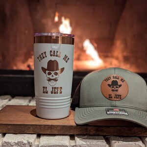 May include: A white tumbler with a brown skull wearing a cowboy hat and the text "They Call Me El Jefe". A green and black baseball cap with a brown leather patch that says "They Call Me El Jefe" with a brown skull wearing a cowboy hat.