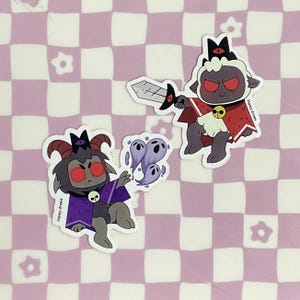 May include: Two cartoon stickers of a black and purple demon with horns and a white sheep with a red cape and a sword. Both characters have red eyes and are wearing crowns. The stickers are on a pink and white checkered background. The text "Haley draws" is on both stickers.