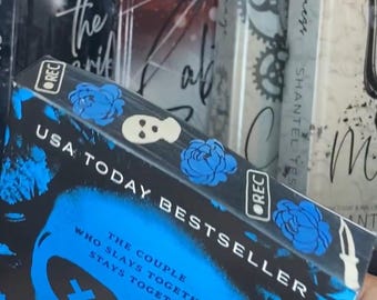 May include: A blue and black paperback book with a skull graphic and the text "The Couple Who Slays Together, Stays Together." The book is titled "Light Out" by Navessa Allen and is a USA Today Bestseller.