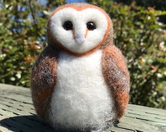 May include: A hand-felted barn owl figurine with brown and white feathers. The owl has a white face with black eyes and a small orange beak.
