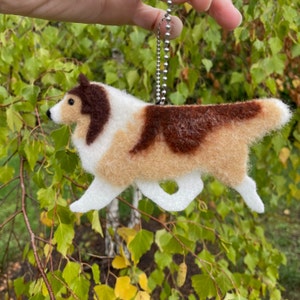 May include: A brown and white felt dog keychain with a silver chain. The dog is a Collie breed and is running.