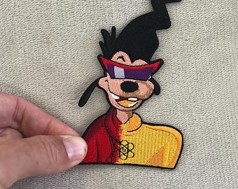 May include: Embroidered patch featuring a cartoon character with black hair, a black hat, and red-purple sunglasses. The character wears a red and yellow jacket with a floral design. The patch is held by a hand.