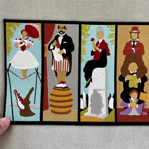 Może przedstawiać: Haftowana naszywka z czterema panelami ze stylizowanymi postaciami. Panele przedstawiają kobietę z parasolem, mężczyznę ze zwojem, kobietę z różą i mężczyznę na innych. Naszywka ma czarną obwódkę i jest przeznaczona na kurtkę lub torbę.