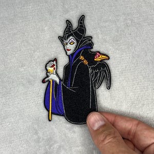 Embroidered patch featuring Maleficent wearing a black robe with purple accents, holding her staff with a raven perched nearby, measuring four inches by two and a half inches.