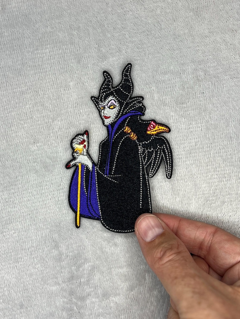 Embroidered patch featuring Maleficent wearing a black robe with purple accents, holding her staff with a raven perched nearby, measuring four inches by two and a half inches.