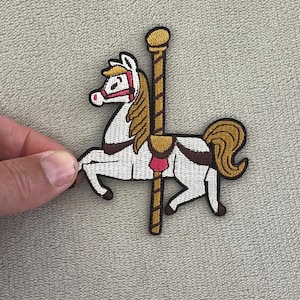 May include: Embroidered patch featuring a carousel horse with a white body, brown mane and tail, and red accents. The patch includes a brown pole and a gold top. This patch is suitable for clothing or accessories.