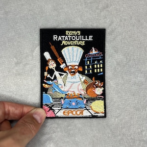 May include: Embroidered patch featuring Remy from Ratatouille, with the text "Remy's Ratatouille Adventure" and "EPCOT". The patch has a black background with colourful illustrations of the chef, food, and buildings.