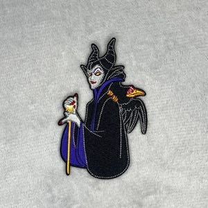 Embroidered patch featuring Maleficent wearing a black robe with purple accents, holding her staff with a raven perched nearby, measuring four inches by two and a half inches.