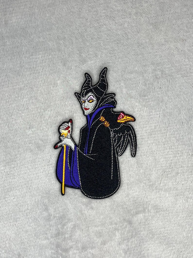 Embroidered patch featuring Maleficent wearing a black robe with purple accents, holding her staff with a raven perched nearby, measuring four inches by two and a half inches.