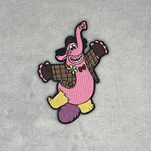 May include: An embroidered patch featuring a pink elephant-like character with a brown plaid jacket, yellow pants, and a purple tail. The character has a small flower on its chest, a red bowtie, and is depicted with arms raised in a joyful pose.