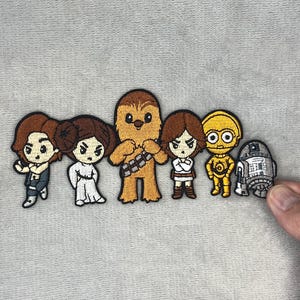 Op de afbeelding: Geborduurde patches met cartoonversies van Star Wars-personages, waaronder Han Solo, prinses Leia en Chewbacca. De patches zijn kleurrijk en gedetailleerd, met verschillende poses en outfits. Geschikt voor kleding of accessoires.