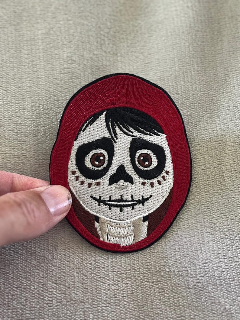 Miguel patch from Coco with painted skull face & red hoodie. 3.5x2.75 inch embroidered iron-on — perfect Disney Día de los Muertos accent.