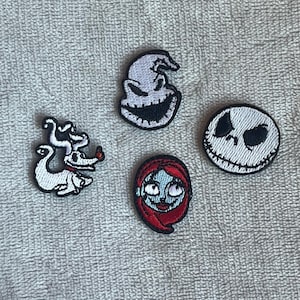 Könnte beinhalten: Vier aufgestickte Aufnäher mit Charakteren aus The Nightmare Before Christmas. Enthält Jack Skellington, Sally, Zero und Oogie Boogie. Jeder Aufnäher hat eine schwarze Umrandung und befindet sich auf grauem Hintergrund.