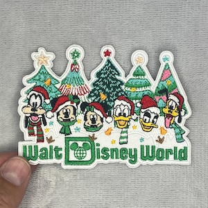 May include: An embroidered patch featuring six Disney characters wearing Santa hats and scarves in front of five stylized Christmas trees. The text Walt Disney World is stitched in green at the bottom, with a Mickey Mouse icon inside the letter D.