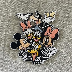 May include: Embroidered patch featuring Mickey Mouse, Minnie Mouse, Donald Duck, Daisy Duck, Goofy, and Pluto. The characters are depicted in a skeleton-like design with white bones and black outlines, with their signature colors.